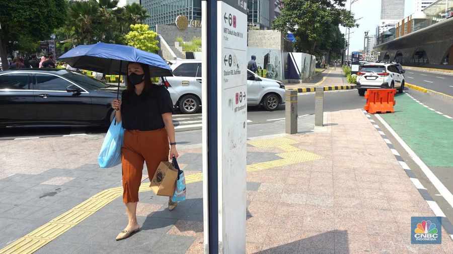 Pejalan kaki menggunakan payung untuk menghindari terik matahari di kawasan Jembatan Pinisi di halte busway Karet, Jakarta, Selasa (19/12/2023). (CNBC Indonesia/Muhammad Sabki)