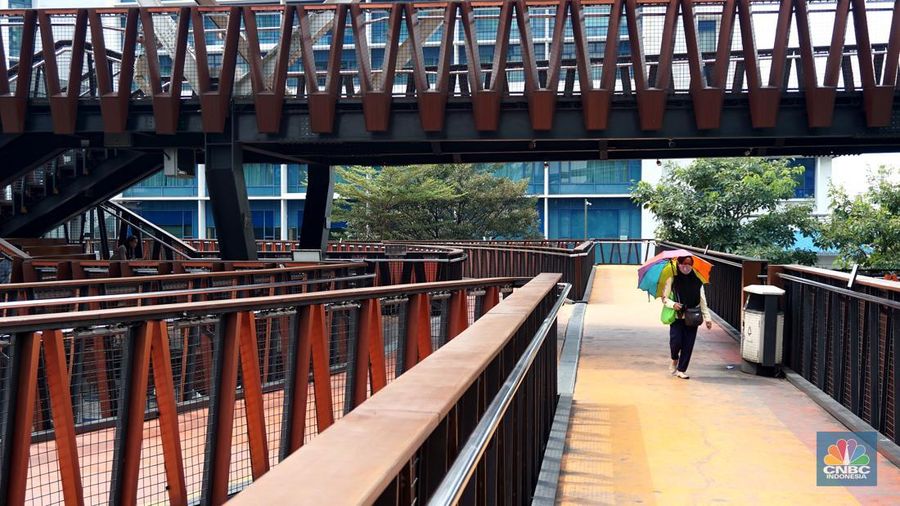 Pejalan kaki menggunakan payung untuk menghindari terik matahari di kawasan Jembatan Pinisi di halte busway Karet, Jakarta, Selasa (19/12/2023). (CNBC Indonesia/Muhammad Sabki)