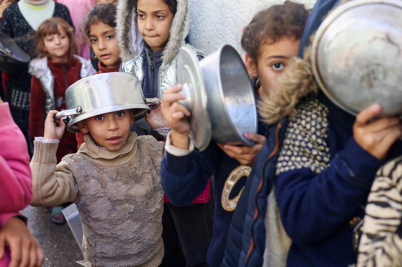 Anak-anak Palestina memegang panci saat mereka mengantri untuk menerima makanan yang dimasak oleh dapur amal, di tengah kekurangan pasokan makanan, saat konflik antara Israel dan Hamas berlanjut, di Rafah di selatan Jalur Gaza 14 Desember 2023. (REUTERS/Saleh Salem)