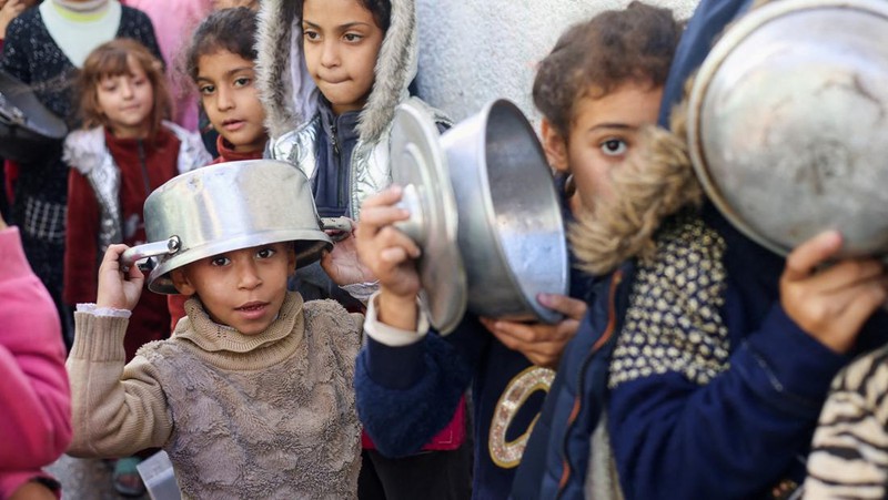 Anak-anak Palestina memegang panci saat mereka mengantri untuk menerima makanan yang dimasak oleh dapur amal, di tengah kekurangan pasokan makanan, saat konflik antara Israel dan Hamas berlanjut, di Rafah di selatan Jalur Gaza 14 Desember 2023. (REUTERS/Saleh Salem)