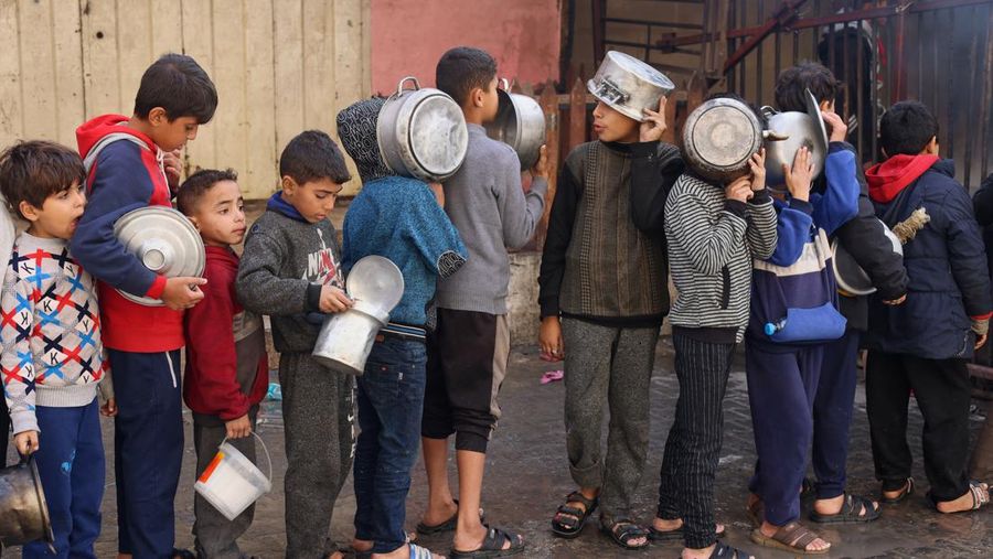 Anak-anak Palestina memegang panci saat mereka mengantri untuk menerima makanan yang dimasak oleh dapur amal, di tengah kekurangan pasokan makanan, saat konflik antara Israel dan Hamas berlanjut, di Rafah di selatan Jalur Gaza 14 Desember 2023. (REUTERS/Saleh Salem)