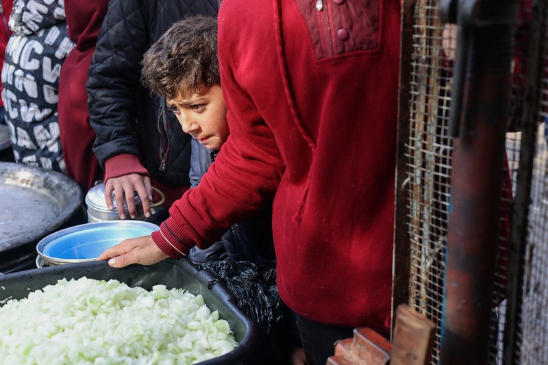 Anak-anak Palestina memegang panci saat mereka mengantri untuk menerima makanan yang dimasak oleh dapur amal, di tengah kekurangan pasokan makanan, saat konflik antara Israel dan Hamas berlanjut, di Rafah di selatan Jalur Gaza 14 Desember 2023. (REUTERS/Saleh Salem)