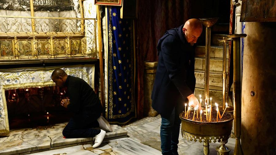 A man prays as another lights a candle in the Church of the Nativity on Christmas Eve, in Bethlehem, in the Israeli-occupied West Bank, December 24, 2023. REUTERS/Clodagh Kilcoyne