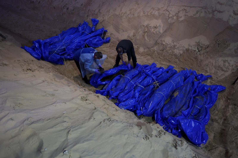 Petugas medis membongkar jenazah warga Palestina yang tewas dalam pertempuran dengan Israel dan diserahkan oleh militer Israel saat pemakaman massal di Rafah, Jalur Gaza, Selasa, 26 Desember 2023. (AP Photo/Fatima Shbair)