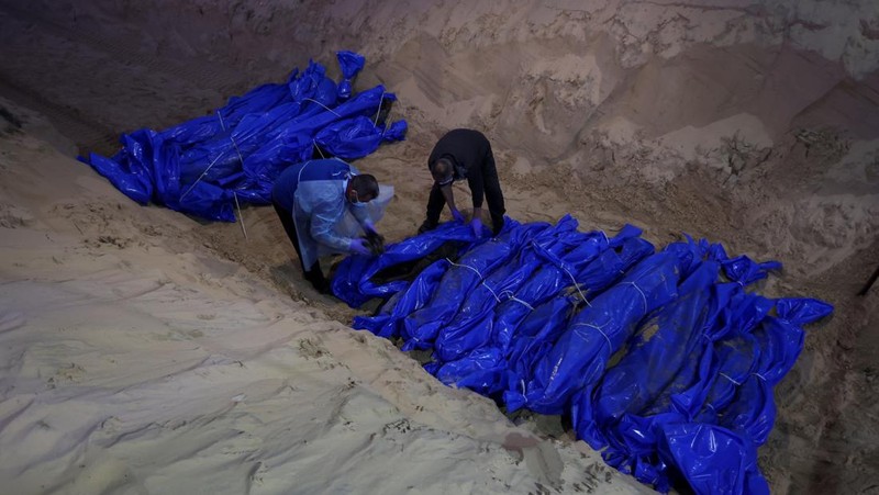Petugas medis membongkar jenazah warga Palestina yang tewas dalam pertempuran dengan Israel dan diserahkan oleh militer Israel saat pemakaman massal di Rafah, Jalur Gaza, Selasa, 26 Desember 2023. (AP Photo/Fatima Shbair)