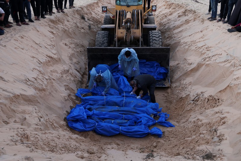 Petugas medis membongkar jenazah warga Palestina yang tewas dalam pertempuran dengan Israel dan diserahkan oleh militer Israel saat pemakaman massal di Rafah, Jalur Gaza, Selasa, 26 Desember 2023. (AP Photo/Fatima Shbair)