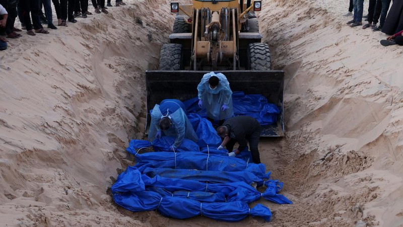 Petugas medis membongkar jenazah warga Palestina yang tewas dalam pertempuran dengan Israel dan diserahkan oleh militer Israel saat pemakaman massal di Rafah, Jalur Gaza, Selasa, 26 Desember 2023. (AP Photo/Fatima Shbair)