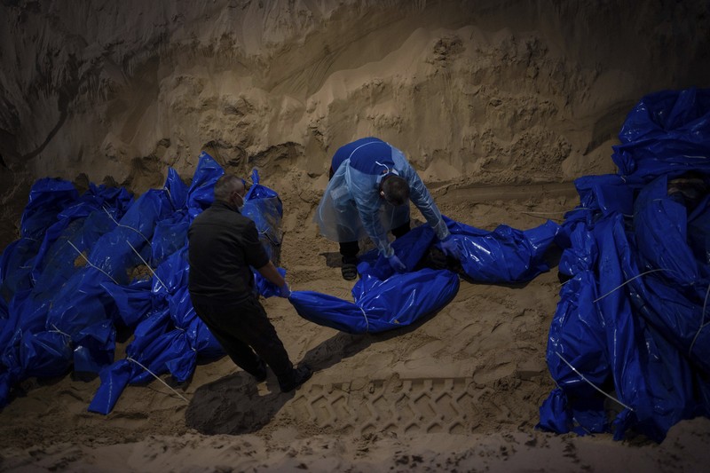 Petugas medis membongkar jenazah warga Palestina yang tewas dalam pertempuran dengan Israel dan diserahkan oleh militer Israel saat pemakaman massal di Rafah, Jalur Gaza, Selasa, 26 Desember 2023. (AP Photo/Fatima Shbair)