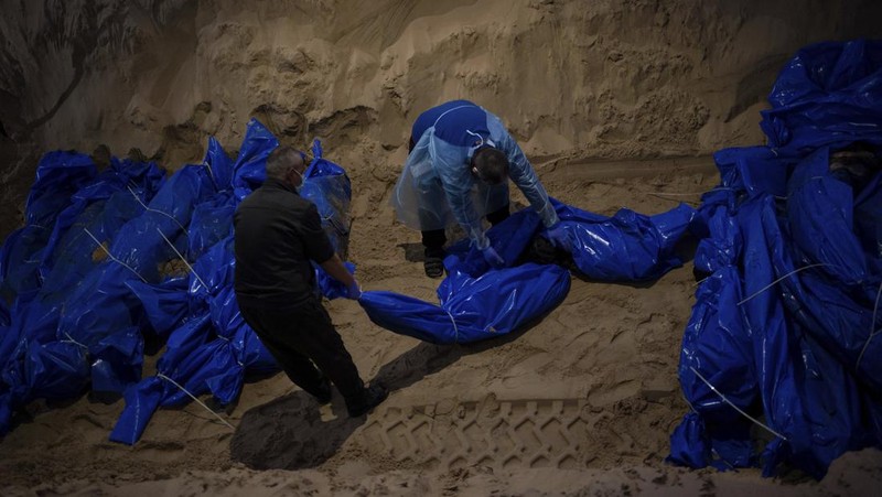 Petugas medis membongkar jenazah warga Palestina yang tewas dalam pertempuran dengan Israel dan diserahkan oleh militer Israel saat pemakaman massal di Rafah, Jalur Gaza, Selasa, 26 Desember 2023. (AP Photo/Fatima Shbair)
