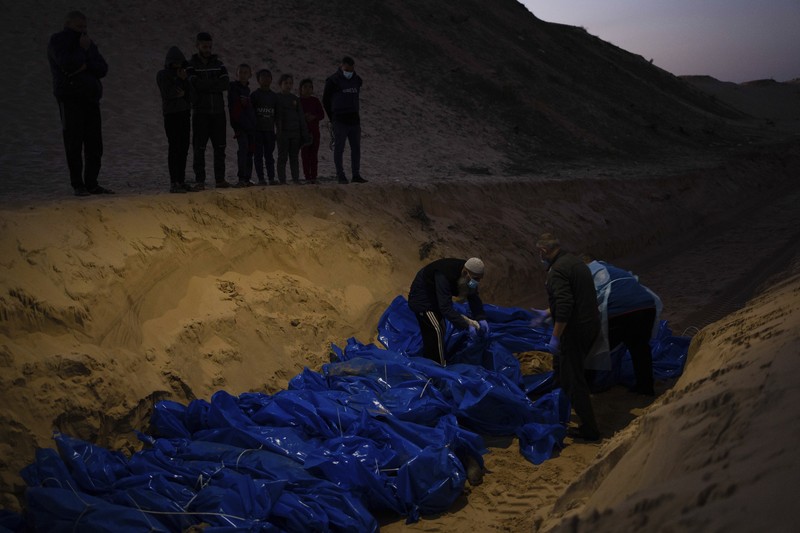 Petugas medis membongkar jenazah warga Palestina yang tewas dalam pertempuran dengan Israel dan diserahkan oleh militer Israel saat pemakaman massal di Rafah, Jalur Gaza, Selasa, 26 Desember 2023. (AP Photo/Fatima Shbair)