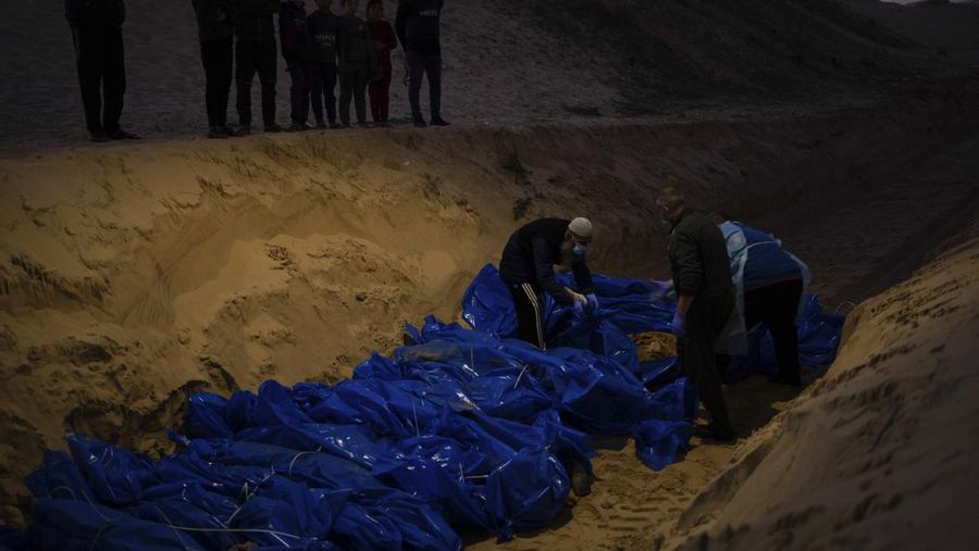 Petugas medis membongkar jenazah warga Palestina yang tewas dalam pertempuran dengan Israel dan diserahkan oleh militer Israel saat pemakaman massal di Rafah, Jalur Gaza, Selasa, 26 Desember 2023. (AP Photo/Fatima Shbair)