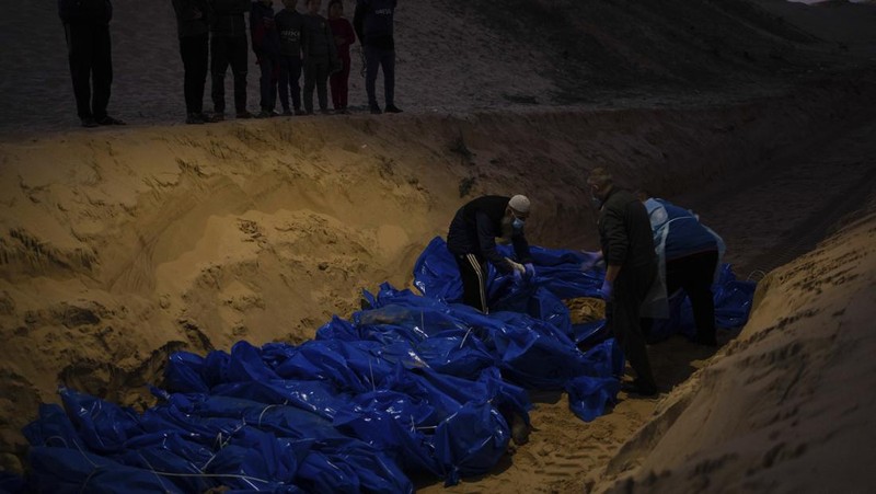 Petugas medis membongkar jenazah warga Palestina yang tewas dalam pertempuran dengan Israel dan diserahkan oleh militer Israel saat pemakaman massal di Rafah, Jalur Gaza, Selasa, 26 Desember 2023. (AP Photo/Fatima Shbair)