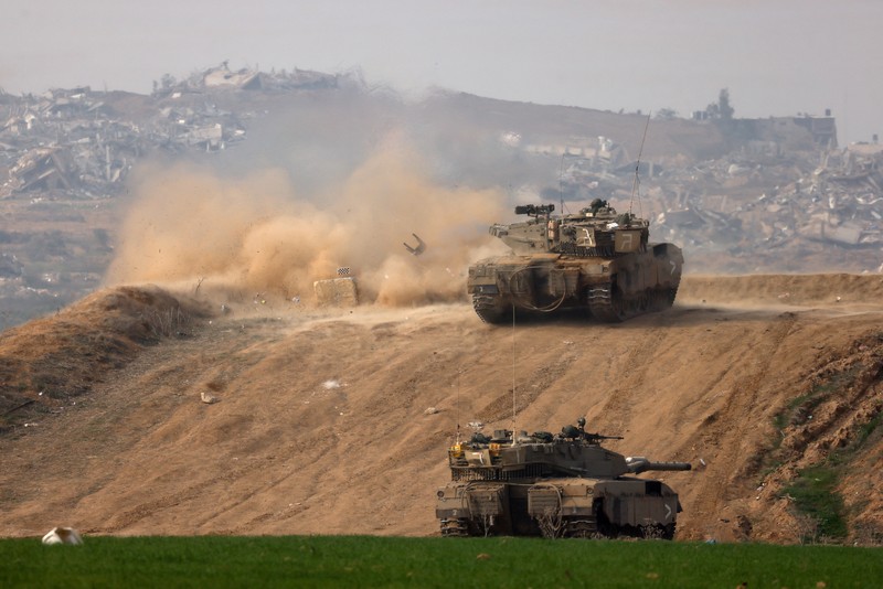 Pria Yahudi ultra-Ortodoks memberi isyarat saat tank Israel melakukan manuver di dekat perbatasan Israel-Gaza, di tengah konflik yang sedang berlangsung antara Israel dan kelompok Islam Palestina Hamas, di Israel selatan, 27 Desember 2023. (REUTERS/Amir Cohen)
