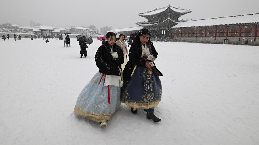 Visitors wearing traditional hanbok dress walk in the snow at Gyeongbokgung palace in central Seoul on December 30, 2023. (JUNG YEON-JE/AFP via Getty Images)