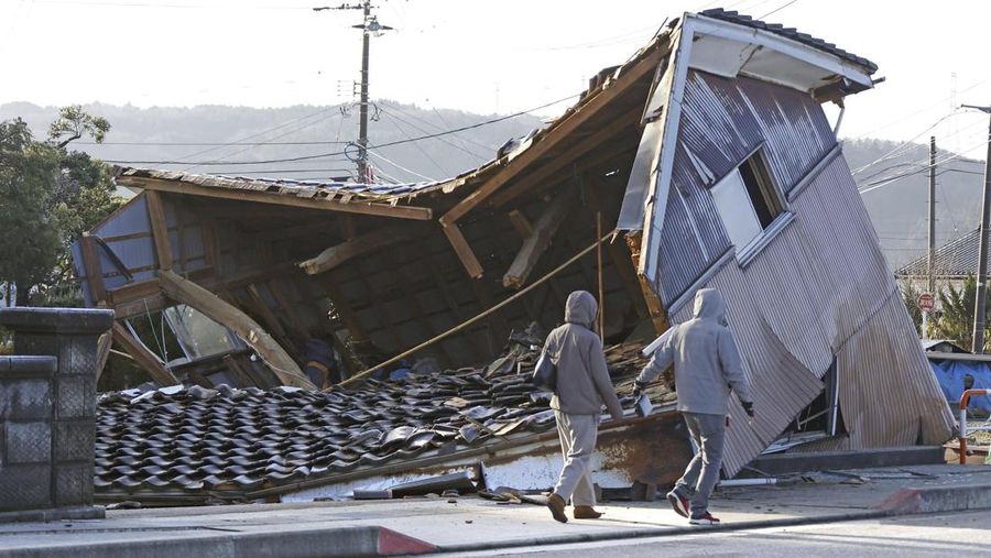 People walk by a building collapsed following an earthquake in Shikamachi, Ishikawa prefecture, Japan Tuesday, Jan. 2, 2024. A series of powerful earthquakes in western Japan damaged homes, cars and boats, with officials warning people on Tuesday to stay away from their homes in some areas because of a continuing risk of major quakes and tsunamis. (Kyodo News via AP)