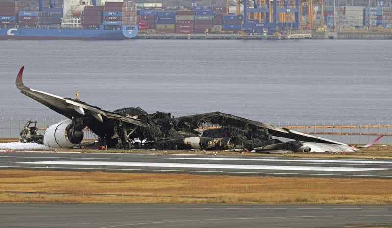 Japan Plane Fire The burn-out Japan Airlines plane is seen, at rear, at Haneda airport on Wednesday, Jan. 3, 2024, in Tokyo, Japan. The large passenger plane and a Japanese coast guard aircraft collided on the runway at Tokyo's Haneda Airport on Tuesday and burst into flames, killing several people aboard the coast guard plane, officials said. (Kyodo News via AP)