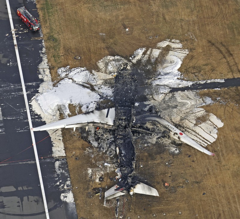 Japan Plane Fire The burn-out Japan Airlines plane is seen, at rear, at Haneda airport on Wednesday, Jan. 3, 2024, in Tokyo, Japan. The large passenger plane and a Japanese coast guard aircraft collided on the runway at Tokyo's Haneda Airport on Tuesday and burst into flames, killing several people aboard the coast guard plane, officials said. (Kyodo News via AP)