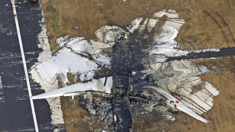 The burn-out Japan Airlines plane is seen, at rear, at Haneda airport on Wednesday, Jan. 3, 2024, in Tokyo, Japan. The large passenger plane and a Japanese coast guard aircraft collided on the runway at Tokyo's Haneda Airport on Tuesday and burst into flames, killing several people aboard the coast guard plane, officials said. (Kyodo News via AP)