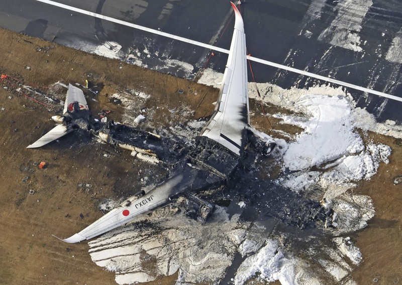 Japan Plane Fire The burn-out Japan Airlines plane is seen, at rear, at Haneda airport on Wednesday, Jan. 3, 2024, in Tokyo, Japan. The large passenger plane and a Japanese coast guard aircraft collided on the runway at Tokyo's Haneda Airport on Tuesday and burst into flames, killing several people aboard the coast guard plane, officials said. (Kyodo News via AP)