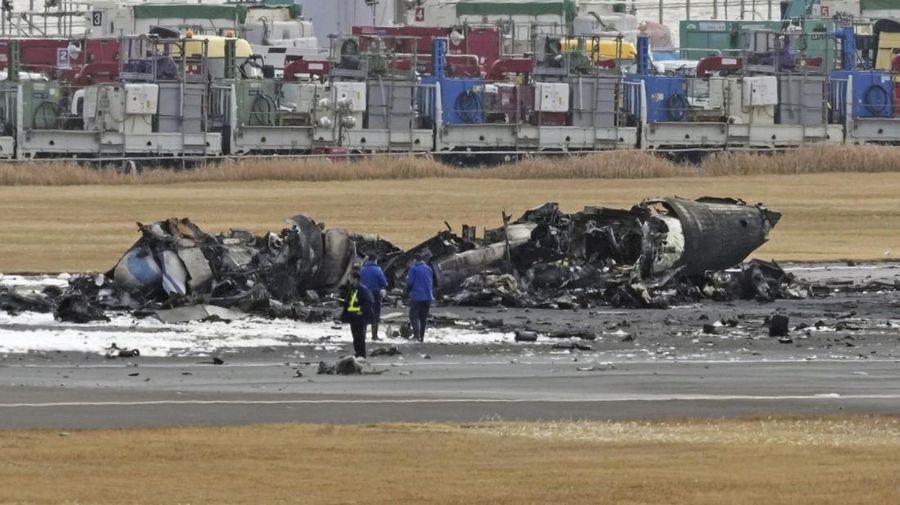 The burn-out Japan Airlines plane is seen, at rear, at Haneda airport on Wednesday, Jan. 3, 2024, in Tokyo, Japan. The large passenger plane and a Japanese coast guard aircraft collided on the runway at Tokyo's Haneda Airport on Tuesday and burst into flames, killing several people aboard the coast guard plane, officials said. (Kyodo News via AP)
