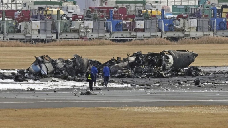 The burn-out Japan Airlines plane is seen, at rear, at Haneda airport on Wednesday, Jan. 3, 2024, in Tokyo, Japan. The large passenger plane and a Japanese coast guard aircraft collided on the runway at Tokyo's Haneda Airport on Tuesday and burst into flames, killing several people aboard the coast guard plane, officials said. (Kyodo News via AP)