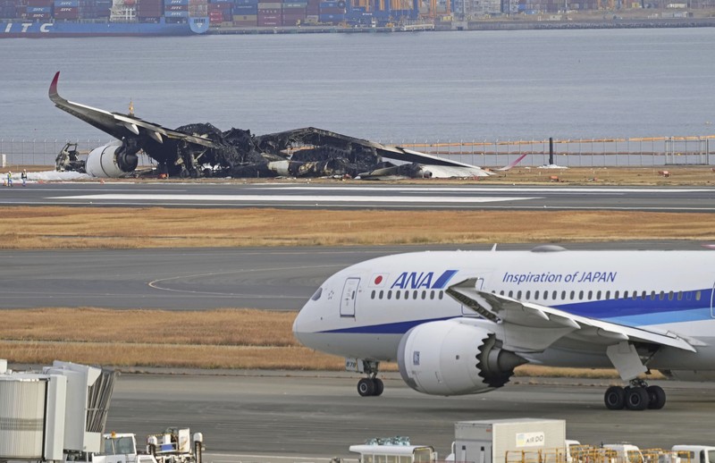 Japan Plane Fire The burn-out Japan Airlines plane is seen, at rear, at Haneda airport on Wednesday, Jan. 3, 2024, in Tokyo, Japan. The large passenger plane and a Japanese coast guard aircraft collided on the runway at Tokyo's Haneda Airport on Tuesday and burst into flames, killing several people aboard the coast guard plane, officials said. (Kyodo News via AP)