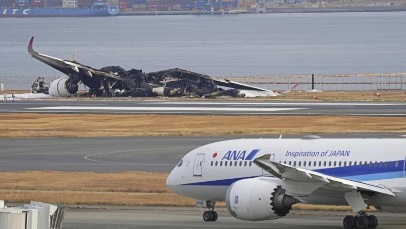 The burn-out Japan Airlines plane is seen, at rear, at Haneda airport on Wednesday, Jan. 3, 2024, in Tokyo, Japan. The large passenger plane and a Japanese coast guard aircraft collided on the runway at Tokyo's Haneda Airport on Tuesday and burst into flames, killing several people aboard the coast guard plane, officials said. (Kyodo News via AP)