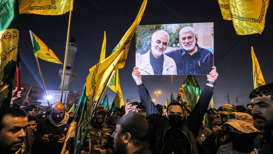 A member of Iraq's Popular Mobilisation Forces (PMF) paramilitaries holds a sign depicting Qasem Soleimani (L), the slain commander of Iran's Islamic Revolutionary Guard Corps' (IRGC) Quds Force, and Iraqi PMF commander Abu Mahdi al-Muhandis, who were killed together by a US drone strike on January 3, 2020; during the funeral of PMF members killed on January 4, 2024 at their headquarters in Baghdad on the same day. A US strike in Baghdad on January 4 killed a military commander of the PMF, an ex-paramilitary faction of the grouping said, with an Iraqi security official reporting two deaths in a drone attack. Harakat al-Nujaba, one of the PMF's factions, said in a statement that