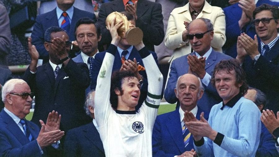 Franz Beckenbauer, tengah, kapten tim tim nasional sepak bola Jerman pemenang kejuaraan sepak bola dunia 1974 menyerahkan trofi di stadion Olimpiade Munich di Jerman, 7 Juli 1974. (AP Photo/stf, File)