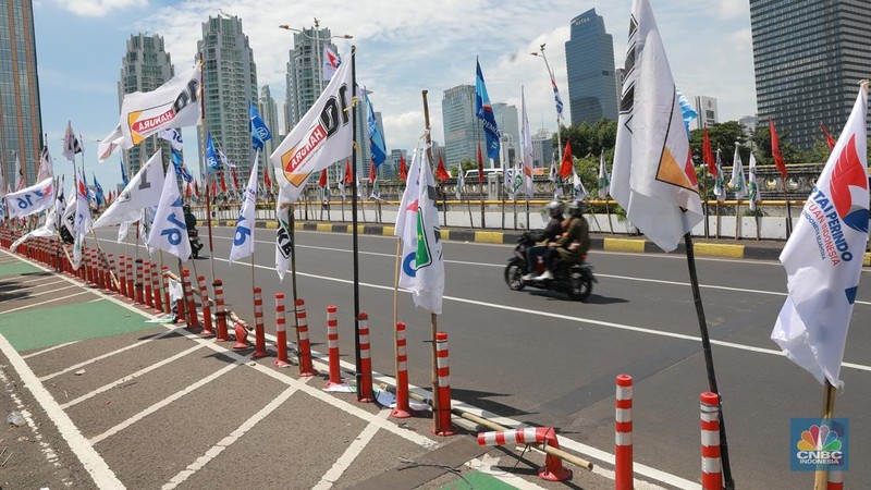 Kendaraan bermotor melintas di samping alat peraga kampanye (APK) pemilu 2024 yang terpasang di pembatas jalur sepeda (stick cone) di kawasan Menteng, Jakarta, Selasa (9/1/2024). Pemasangan APK Pemilu 2024 tersebut melanggar Peraturan KPU yang melarang pemasangan atribut partai atau caleg di fasilitas umum. (CNBC Indonesia/Muhammad Sabki)