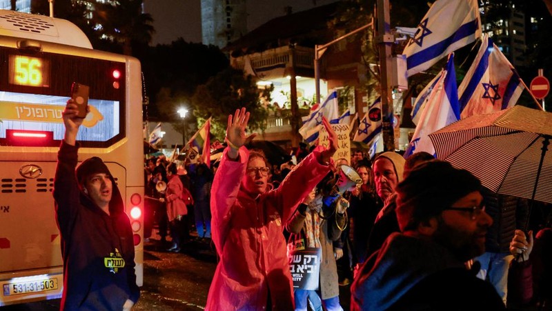 Seorang pengunjuk rasa berdiri di samping spanduk bergambar Perdana Menteri Israel Benjamin Netanyahu saat ia menghadiri rapat umum yang menuntut gencatan senjata segera di Gaza, di tengah konflik yang sedang berlangsung antara Israel dan kelompok Islam Palestina Hamas, di Tel Aviv, Israel, 27 Januari. 2024. (REUTERS/Tyrone Siu)