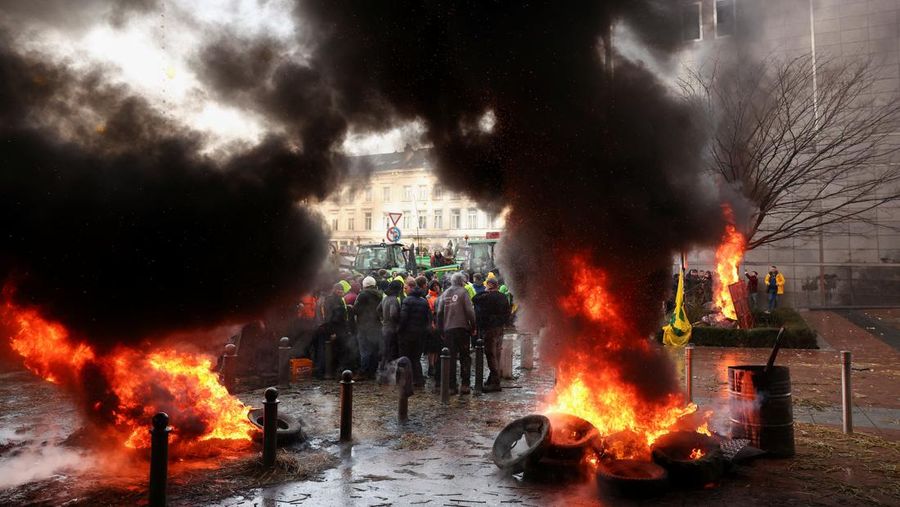 Asap mengepul dari benda-benda yang dibakar ketika orang-orang berkumpul di depan kantor pusat Uni Eropa ketika para petani Belgia menggunakan traktor mereka untuk memblokir kantor pusat, ketika mereka memprotes tekanan harga, pajak dan peraturan ramah lingkungan, keluhan yang dirasakan oleh para petani di seluruh Eropa, di Brussels, Belgia 1 Februari 2024. (REUTERS/Yves Herman)