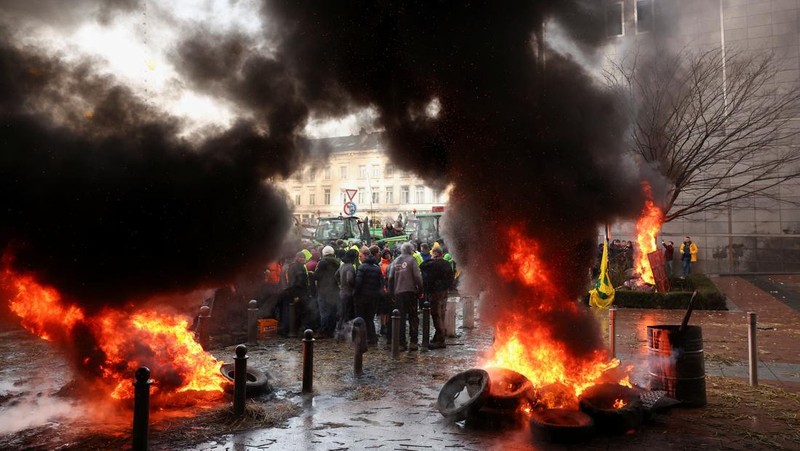 Asap mengepul dari benda-benda yang dibakar ketika orang-orang berkumpul di depan kantor pusat Uni Eropa ketika para petani Belgia menggunakan traktor mereka untuk memblokir kantor pusat, ketika mereka memprotes tekanan harga, pajak dan peraturan ramah lingkungan, keluhan yang dirasakan oleh para petani di seluruh Eropa, di Brussels, Belgia 1 Februari 2024. (REUTERS/Yves Herman)