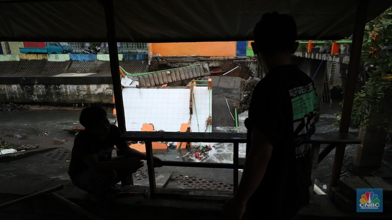 Warga mengamati Pos Pintu Air Palmerah yang jebol di kawasan Palmerah, Jakarta Barat, Selasa (6/2/2024). (CNBC Indonesia/Tri Susilo)