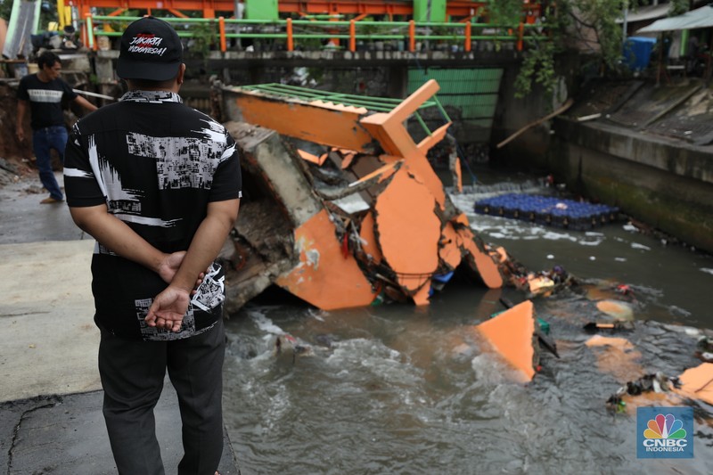 Warga mengamati Pos Pintu Air Palmerah yang jebol di kawasan Palmerah, Jakarta Barat, Selasa (6/2/2024). (CNBC Indonesia/Tri Susilo)