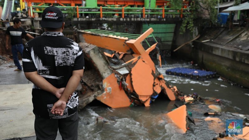 Warga mengamati Pos Pintu Air Palmerah yang jebol di kawasan Palmerah, Jakarta Barat, Selasa (6/2/2024). (CNBC Indonesia/Tri Susilo)