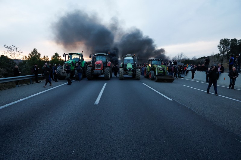 EUROPE-FARMERS/SPAIN Demonstrators stand next to tractors, as farmers block the AP-7 highway during a protest over price pressures, taxes and green regulation, grievances shared by farmers across Europe, near Girona, Spain, February 6, 2024. REUTERS/Albert Gea
