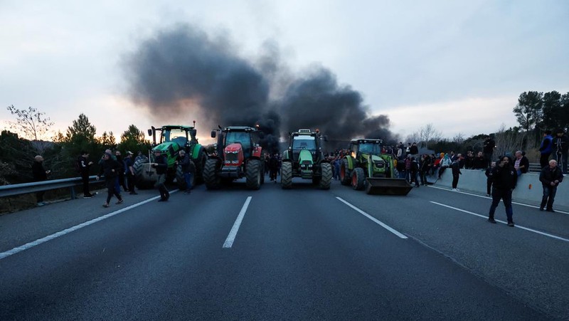 Demonstrators stand next to tractors, as farmers block the AP-7 highway during a protest over price pressures, taxes and green regulation, grievances shared by farmers across Europe, near Girona, Spain, February 6, 2024. REUTERS/Albert Gea