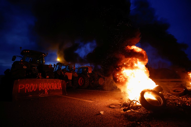 EUROPE-FARMERS/SPAIN Demonstrators stand next to tractors, as farmers block the AP-7 highway during a protest over price pressures, taxes and green regulation, grievances shared by farmers across Europe, near Girona, Spain, February 6, 2024. REUTERS/Albert Gea