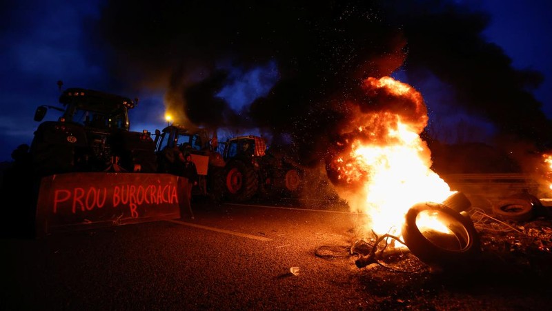 Demonstrators stand next to tractors, as farmers block the AP-7 highway during a protest over price pressures, taxes and green regulation, grievances shared by farmers across Europe, near Girona, Spain, February 6, 2024. REUTERS/Albert Gea
