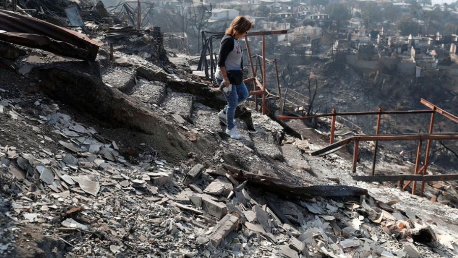 Seorang warga berjalan di atas sisa-sisa bangunan rumahnya yang terbakar akibat meluasnya kebakaran hutan di Vina del Mar, Chili, Senin (5/2/2024). (REUTERS/Rodrigo Garrido)