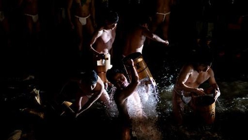 Para pria membersihkan tubuh mereka di sungai selama Festival Sominsai di Kuil Kokuseki-ji di Oshu, Prefektur Iwate, Jepang, pada 17 Februari 2024. (Photo by Philip FONG / AFP)