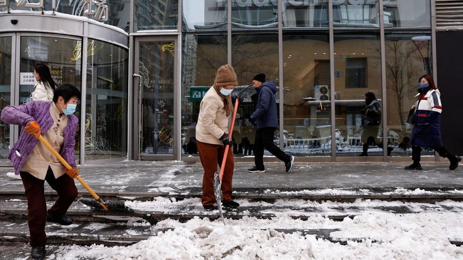 Pekerja membersihkan salju di dekat pusat perbelanjaan setelah hujan salju di Beijing, Cina, 21 Februari 2024. (REUTERS/Tingshu Wang)