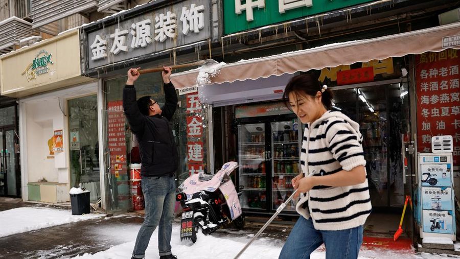 Pemilik toko membersihkan salju di bagian depan setelah hujan salju di Beijing, Cina, 21 Februari 2024. (REUTERS/Tingshu Wang)