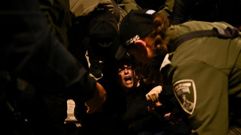 People stand on a street as police use water cannons to disperse demonstrators during a protest against Israeli Prime Minister Benjamin Netanyahu's government, amid the ongoing conflict between Israel and the Palestinian Islamist group Hamas from Gaza, in Tel Aviv, Israel, February 24, 2024. REUTERS/Dylan Martinez