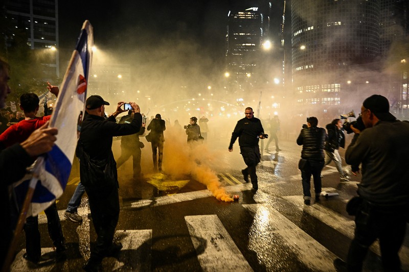 ISRAEL-PALESTINIANS/NETANYAHU-PROTEST People stand on a street as police use water cannons to disperse demonstrators during a protest against Israeli Prime Minister Benjamin Netanyahu's government, amid the ongoing conflict between Israel and the Palestinian Islamist group Hamas from Gaza, in Tel Aviv, Israel, February 24, 2024. REUTERS/Dylan Martinez