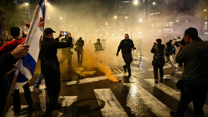 People stand on a street as police use water cannons to disperse demonstrators during a protest against Israeli Prime Minister Benjamin Netanyahu's government, amid the ongoing conflict between Israel and the Palestinian Islamist group Hamas from Gaza, in Tel Aviv, Israel, February 24, 2024. REUTERS/Dylan Martinez