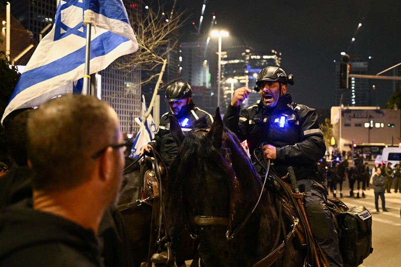 People stand on a street as police use water cannons to disperse demonstrators during a protest against Israeli Prime Minister Benjamin Netanyahu's government, amid the ongoing conflict between Israel and the Palestinian Islamist group Hamas from Gaza, in Tel Aviv, Israel, February 24, 2024. REUTERS/Dylan Martinez