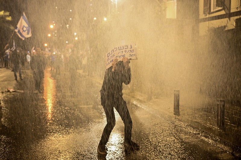 ISRAEL-PALESTINIANS/NETANYAHU-PROTEST People stand on a street as police use water cannons to disperse demonstrators during a protest against Israeli Prime Minister Benjamin Netanyahu's government, amid the ongoing conflict between Israel and the Palestinian Islamist group Hamas from Gaza, in Tel Aviv, Israel, February 24, 2024. REUTERS/Dylan Martinez