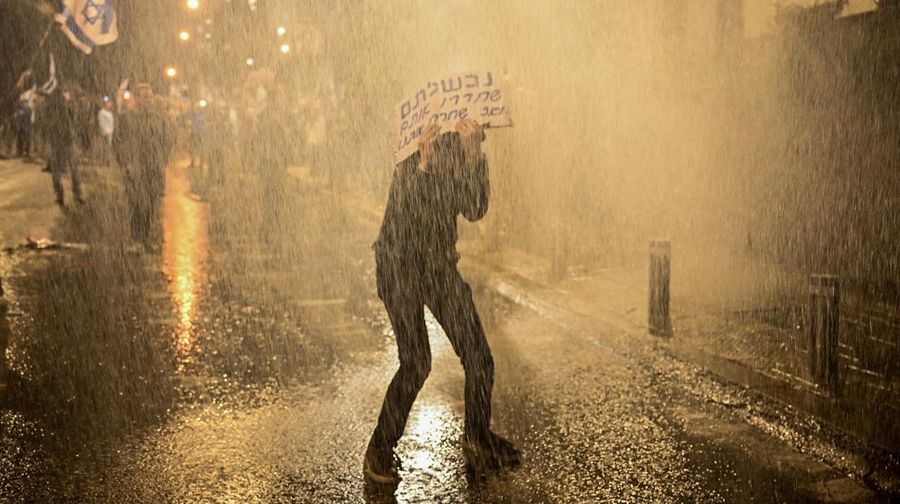 People stand on a street as police use water cannons to disperse demonstrators during a protest against Israeli Prime Minister Benjamin Netanyahu's government, amid the ongoing conflict between Israel and the Palestinian Islamist group Hamas from Gaza, in Tel Aviv, Israel, February 24, 2024. REUTERS/Dylan Martinez